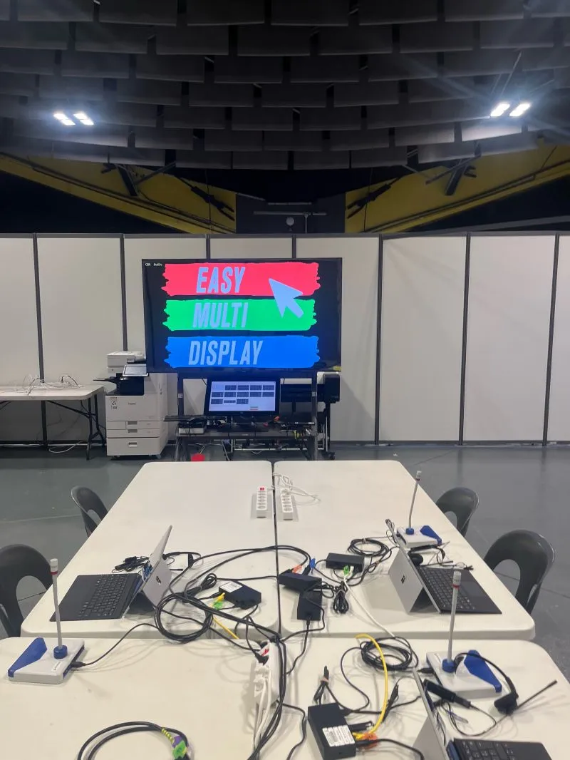 Temporary control room at Lourdes 2026: two laptops and microphones on the table, the touch screen driving the HDMI Multiprise and the Easy Multi Display welcome screen