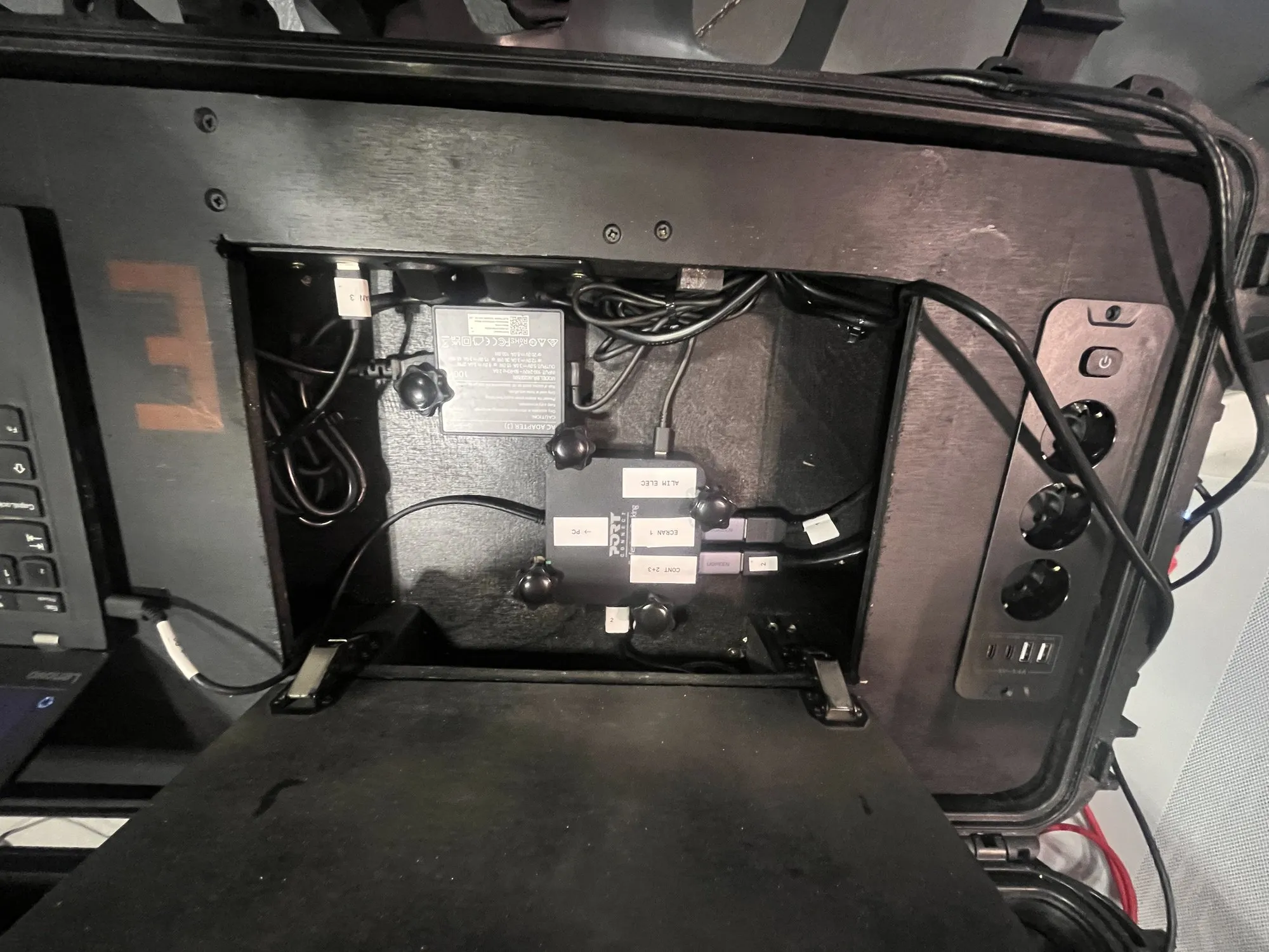 Trampilla técnica vista desde arriba: fuentes de alimentación fijadas y cableadas, tomas de corriente y USB en el lateral de la maleta