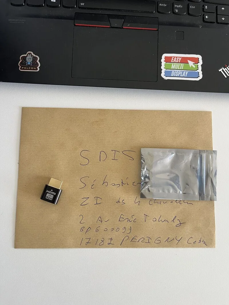 Une enveloppe kraft adressée au SDIS 17, un HDMI dummy plug 4K posé dessus, devant un ordinateur portable frappé du logo Easy Multi Display